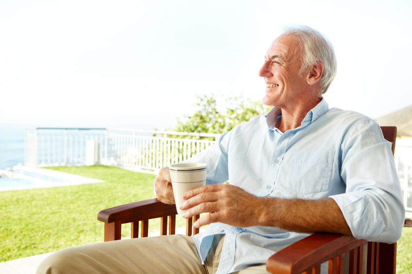 A smiling mature man sitting on a chair outside while looking at the view and drinking tea
