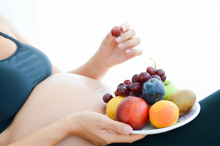 Pregnant woman holding fruits on a plate in front of her belly